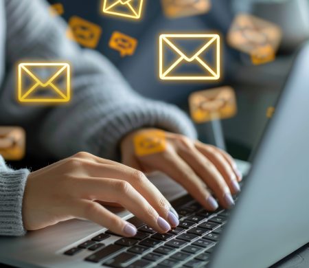 A person works on their computer, emails pouring in from the screen.